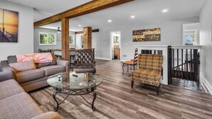 A spacious living area with a wooden ceiling, a glass coffee table, a leather armchair, and a patterned armchair.