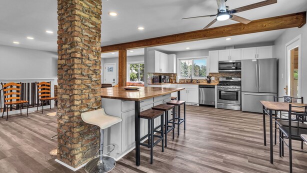 A spacious kitchen with a central island, wooden beams, and a stone pillar.