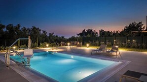 A swimming pool with lounge chairs and a small deck area, surrounded by a fence and trees.