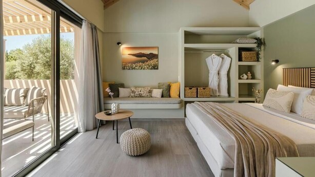 A modern bedroom with a large bed, a seating area with a sofa and chairs, a small round table, and a wardrobe.