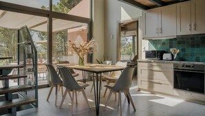 A modern kitchen with large windows, a dining area with a table and chairs, and a view of the outdoors.