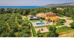 A Mediterranean-style villa with a swimming pool, outdoor seating, and a view of the sea.