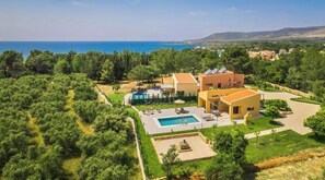 A Mediterranean-style villa with a swimming pool, outdoor seating, and a view of the sea.