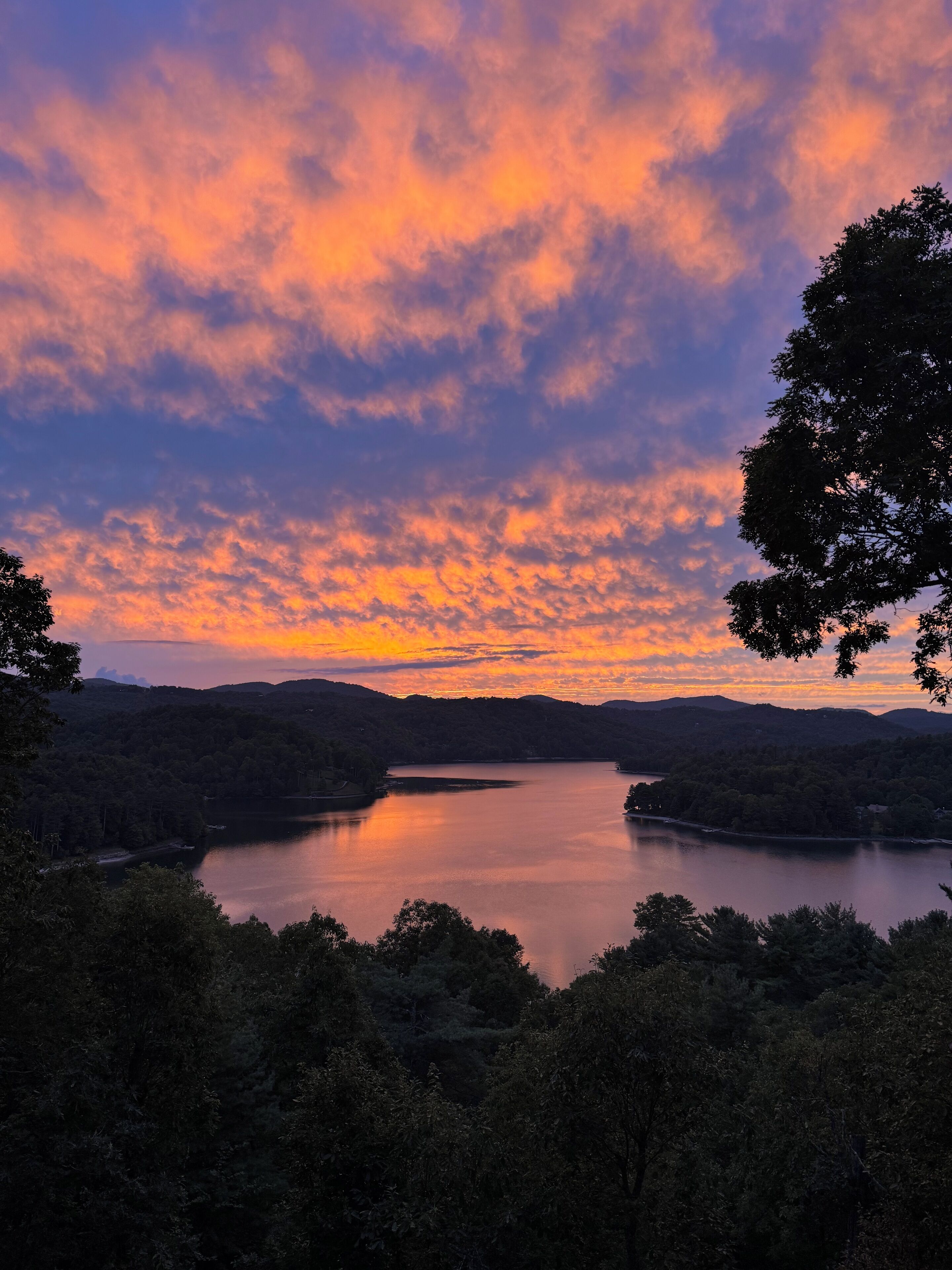 A lake surrounded by forested hills during sunset.