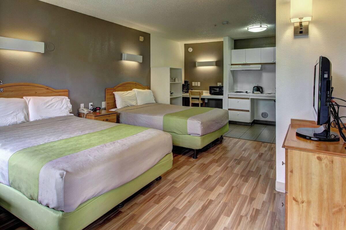 Ein Hotelzimmer mit zwei Betten, einem Schreibtisch, einem Computer, einer Mikrowelle und einer Kaffeemaschine.