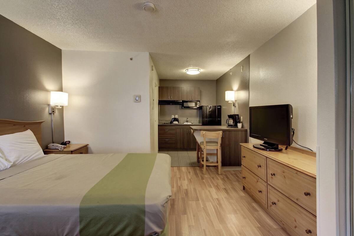 Ein Hotelzimmer mit Bett, Schreibtisch, Stuhl, Fernseher und einer Küchenzeile.