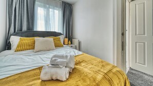 Ein ordentlich bezogenes Bett mit gelber Tagesdecke, Kissen und gefalteten Handtüchern.