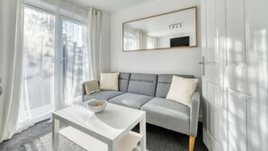 Ein modernes Zimmer mit grauem Sofa, weißem Tisch mit einer Schale, großem Spiegel und einer Schiebeglastür.