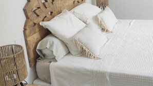 A bed with a wooden headboard, white bedding, and a woven chair. - House for 6 people, 3 bedrooms, 2 bathrooms, 3 WCs, swimming pool, air conditioning and mosquito nets. (Perpignan)