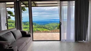 A room with a sofa and a large sliding glass door leading to a scenic view. - Ocean View House - Monteverde (Sierra)