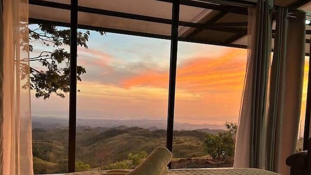 A bedroom with a large bed, a view of the landscape through floor-to-ceiling windows, and a neatly made bed with towels. - Ocean View House - Monteverde (Sierra)