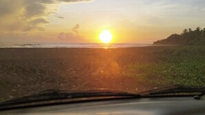 A sunset over a beach with a car dashboard in the foreground. - RELAX IN WARM ROOMS AND SPACE TO REST COMFORTABLY. (León)