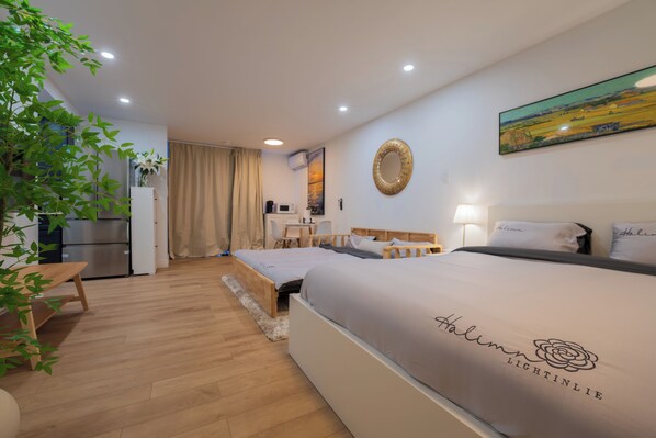 A hotel room with a bed, a desk, a chair, a plant, and a painting on the wall.
