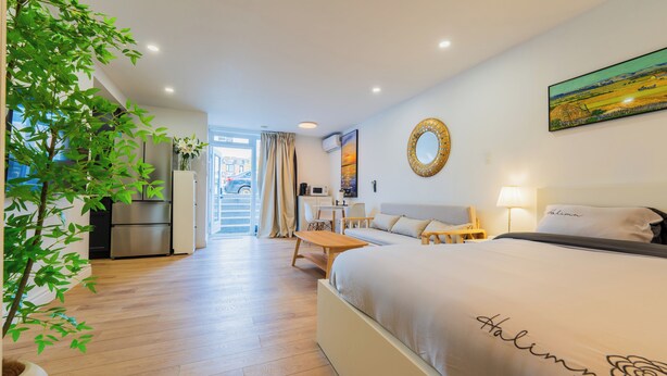 A hotel room with a large bed, a desk, a chair, a potted plant, and a view of the outside. - Spacious Studio for 4 | Full Kitchen + Laundry (Montréal)