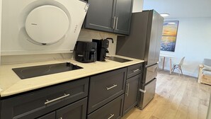A modern kitchen with dark cabinetry, a white refrigerator, a coffee maker, and a sink. - Spacious Studio for 4 | Full Kitchen + Laundry (Montréal)