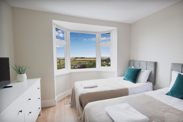 Une chambre avec deux lits, un téléviseur posé sur une commode et une vue sur un paysage grâce à une grande baie vitrée.