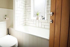 Et badeværelse med et hvidt toilet, et vindue med udsigt til planternes og en trædør.