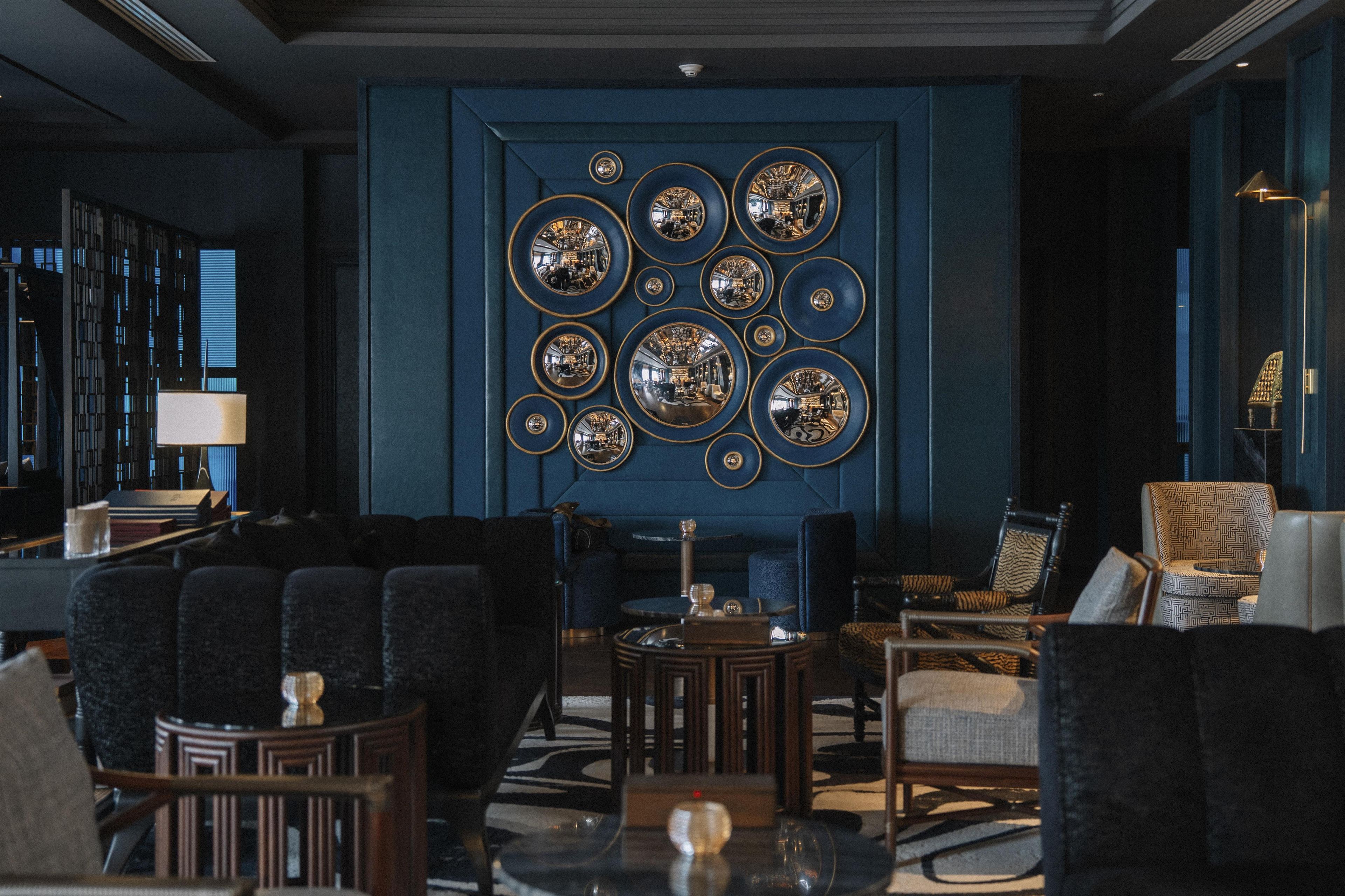 A modern lounge with a blue accent wall, multiple seating areas, and a decorative mirror arrangement.