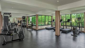 Une salle de sport moderne équipée de machines de cardio, de postes de musculation et de grandes fenêtres donnant sur un espace verdoyant.