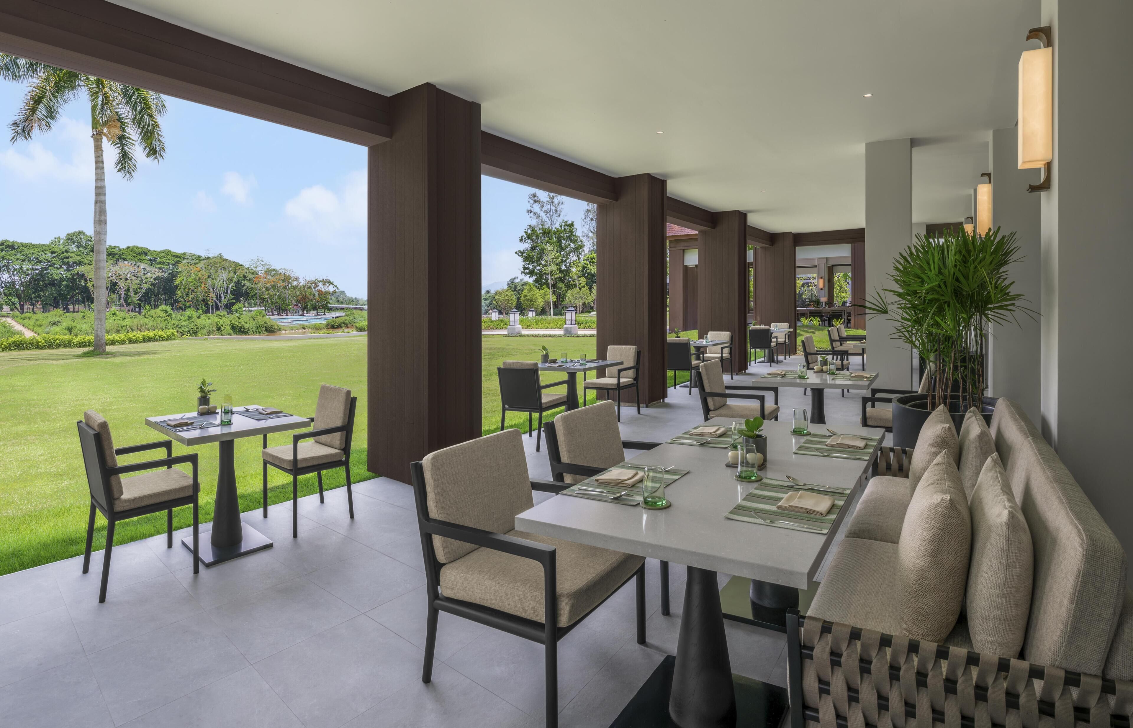 Zona pranzo con tavoli e sedie, un divano e vista su un paesaggio verde.