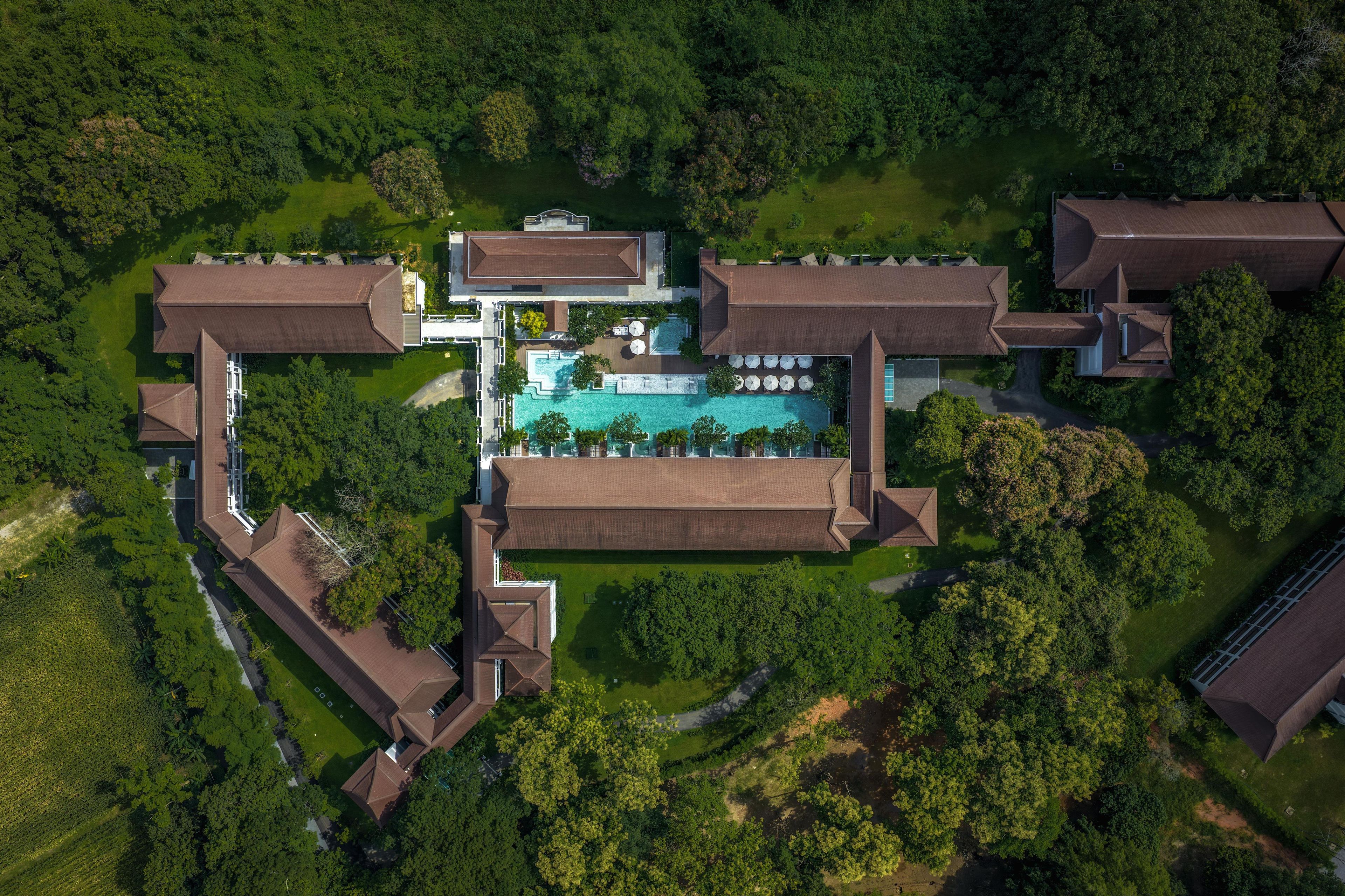 Vista aérea de un complejo turístico con una piscina central, varias edificaciones para huéspedes y vegetación circundante.