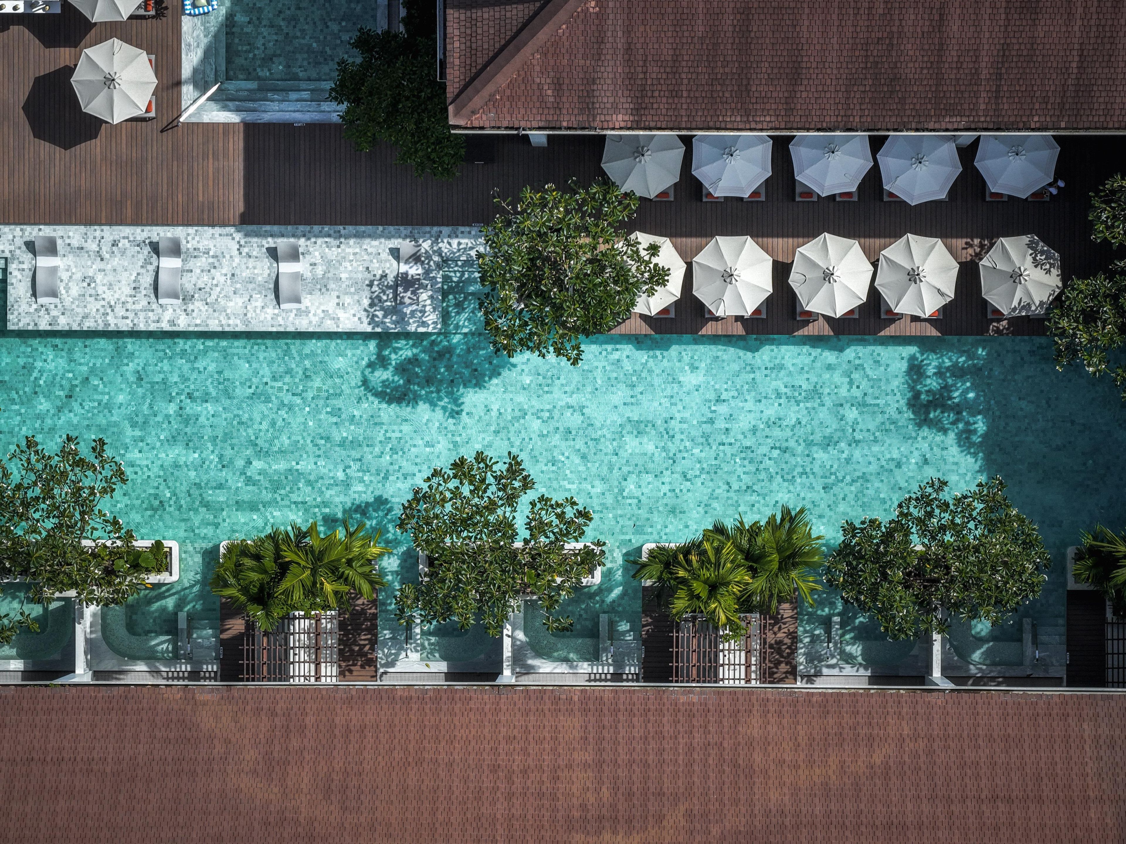 An aerial view of a resort with a swimming pool, lounge area, and umbrellas.