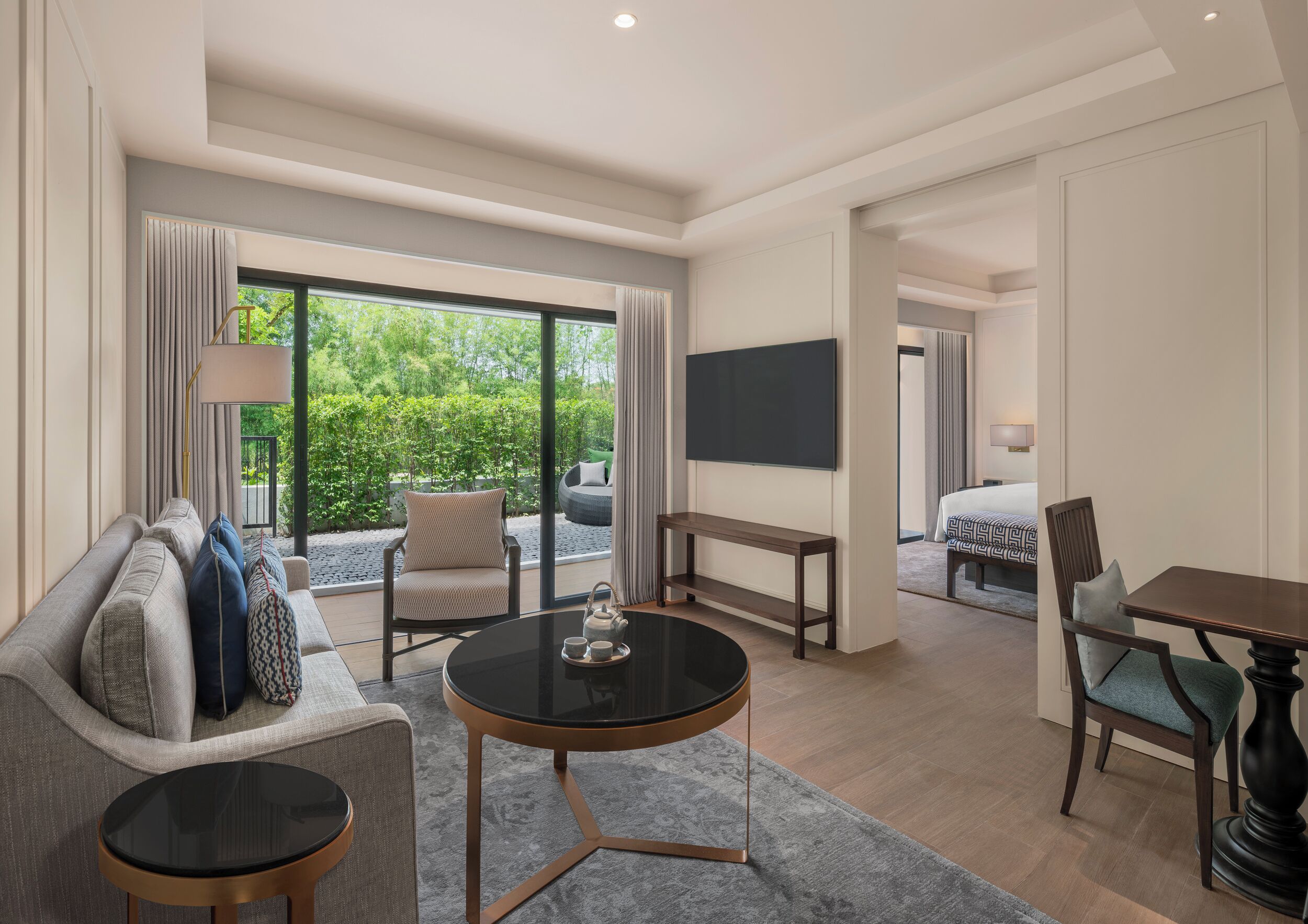 A modern hotel room with a sofa, a round coffee table, a TV, and a bed.