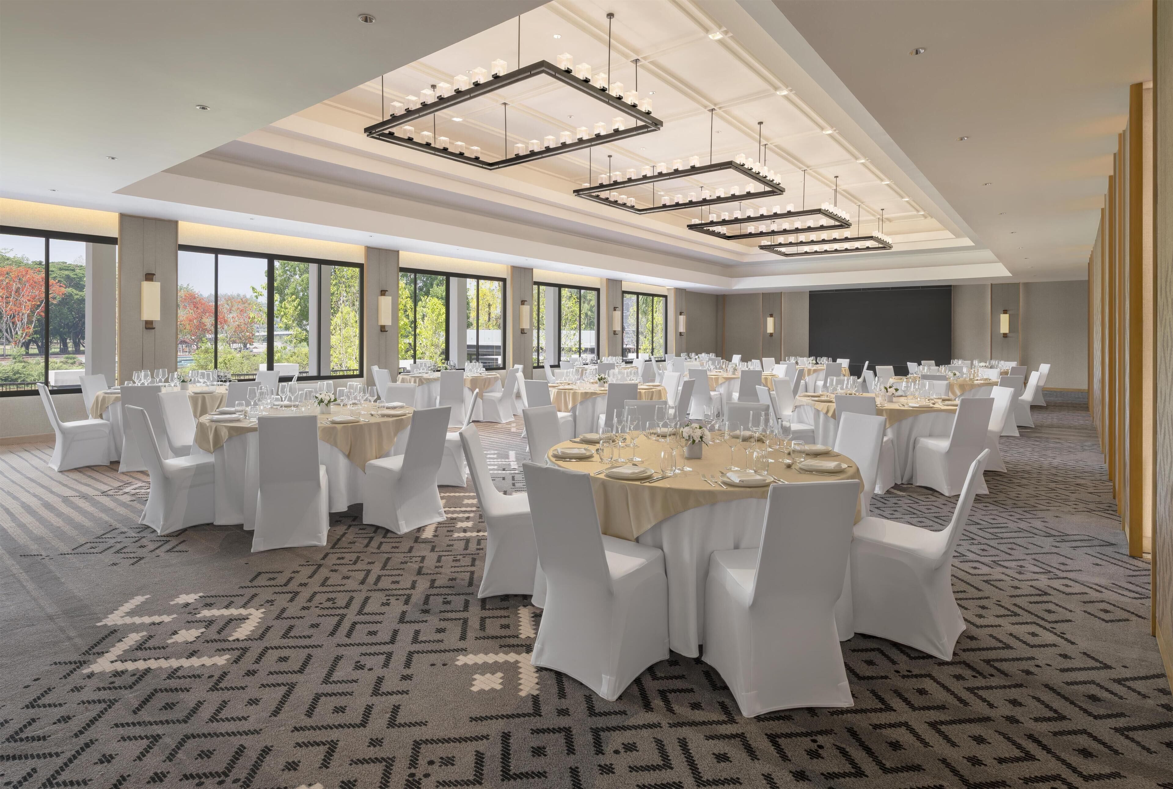 Un amplio salón de conferencias con varias mesas redondas, sillas blancas y candelabros.