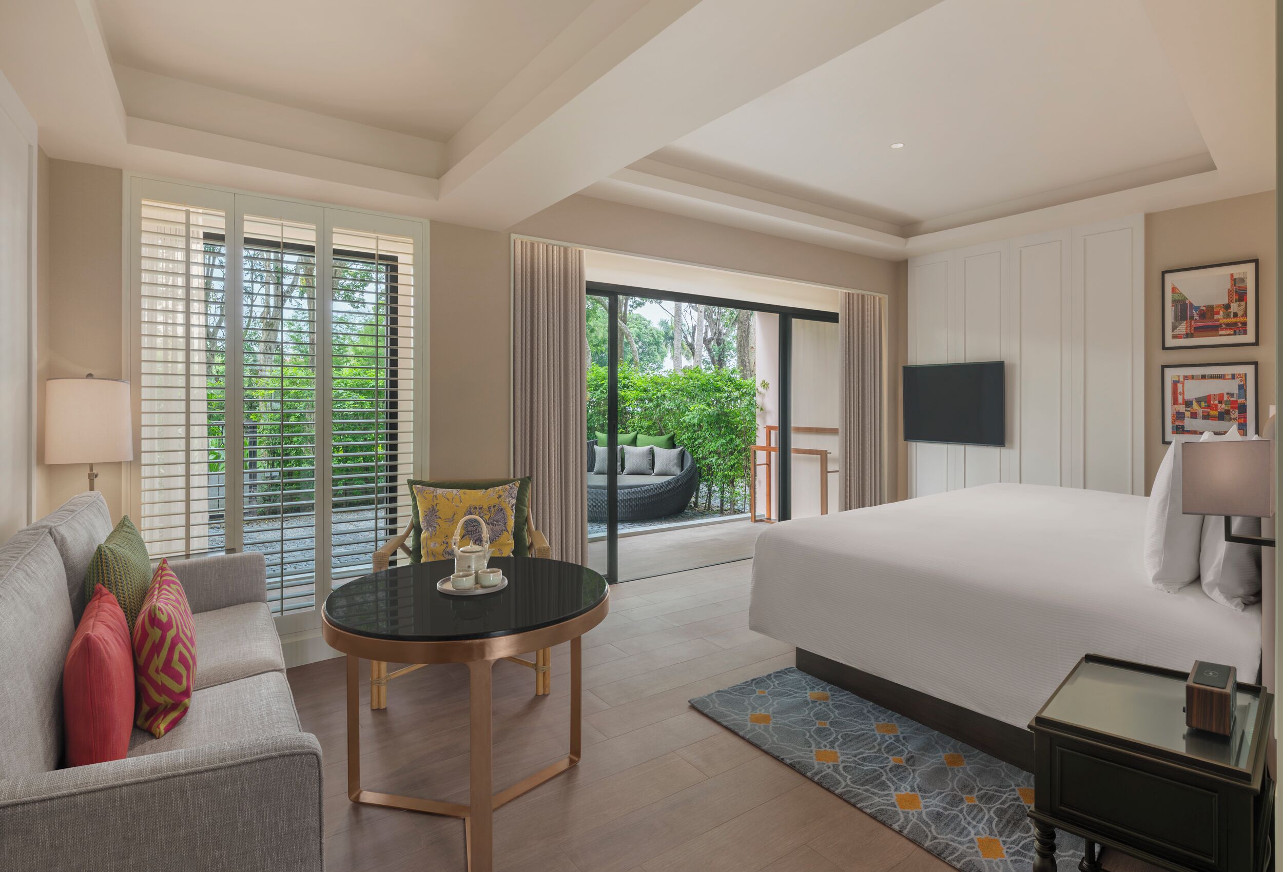 Une chambre d’hôtel comprenant un lit, un canapé, une table, une télévision et un balcon avec vue sur la verdure.