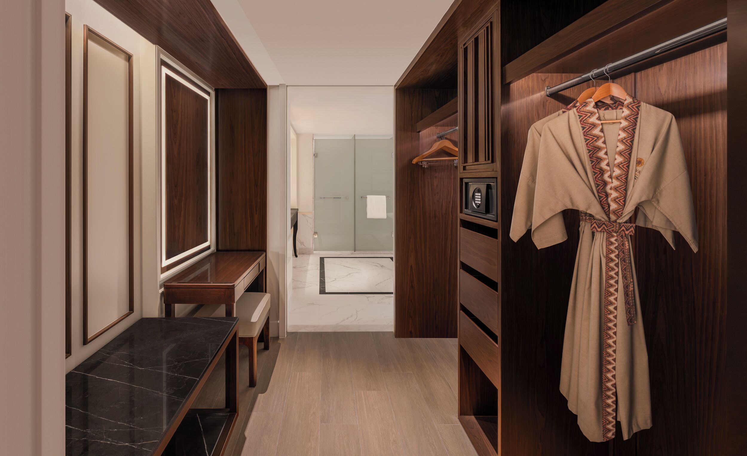 A hallway with wooden paneling, a bench, a coat rack with a robe, and a door leading to a bathroom.