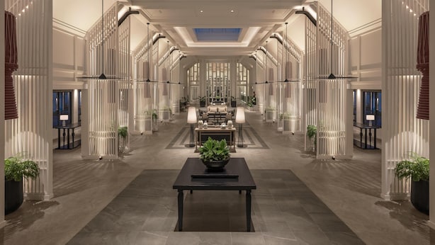A hotel lobby with a central seating area, a ceiling skylight, and symmetrical columns. - Kahavadi Chiang Rai, Curio Collection By Hilton (Chiang Rai)