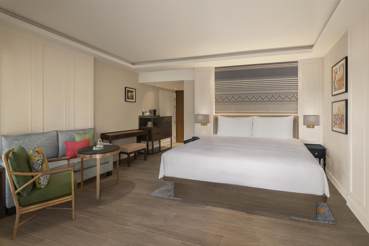 A hotel room with a large bed, a sofa, a small table, and a desk.