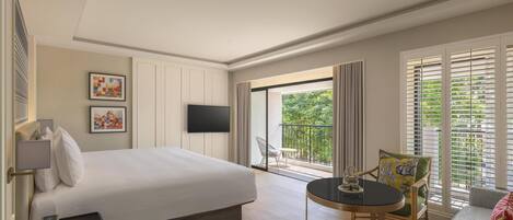 A modern hotel room with a large bed, a flat-screen TV, a balcony with a view of greenery, and a small round table with a chair.
