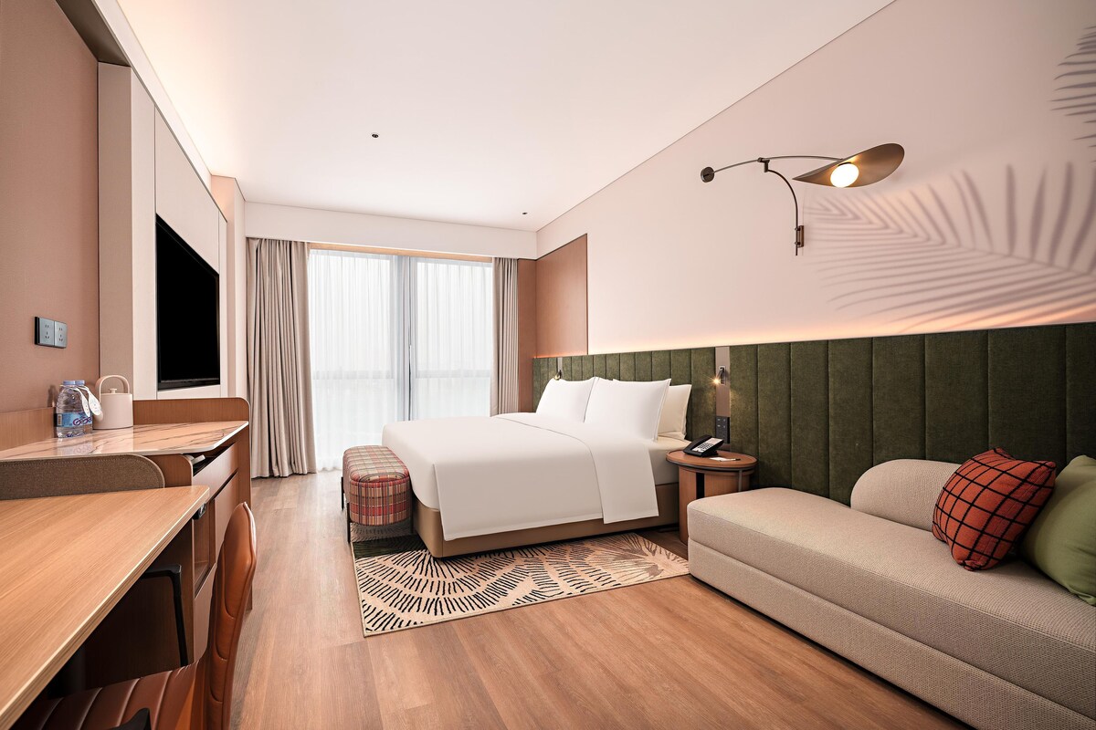 A hotel room with a bed, a sofa, a desk, and a TV.