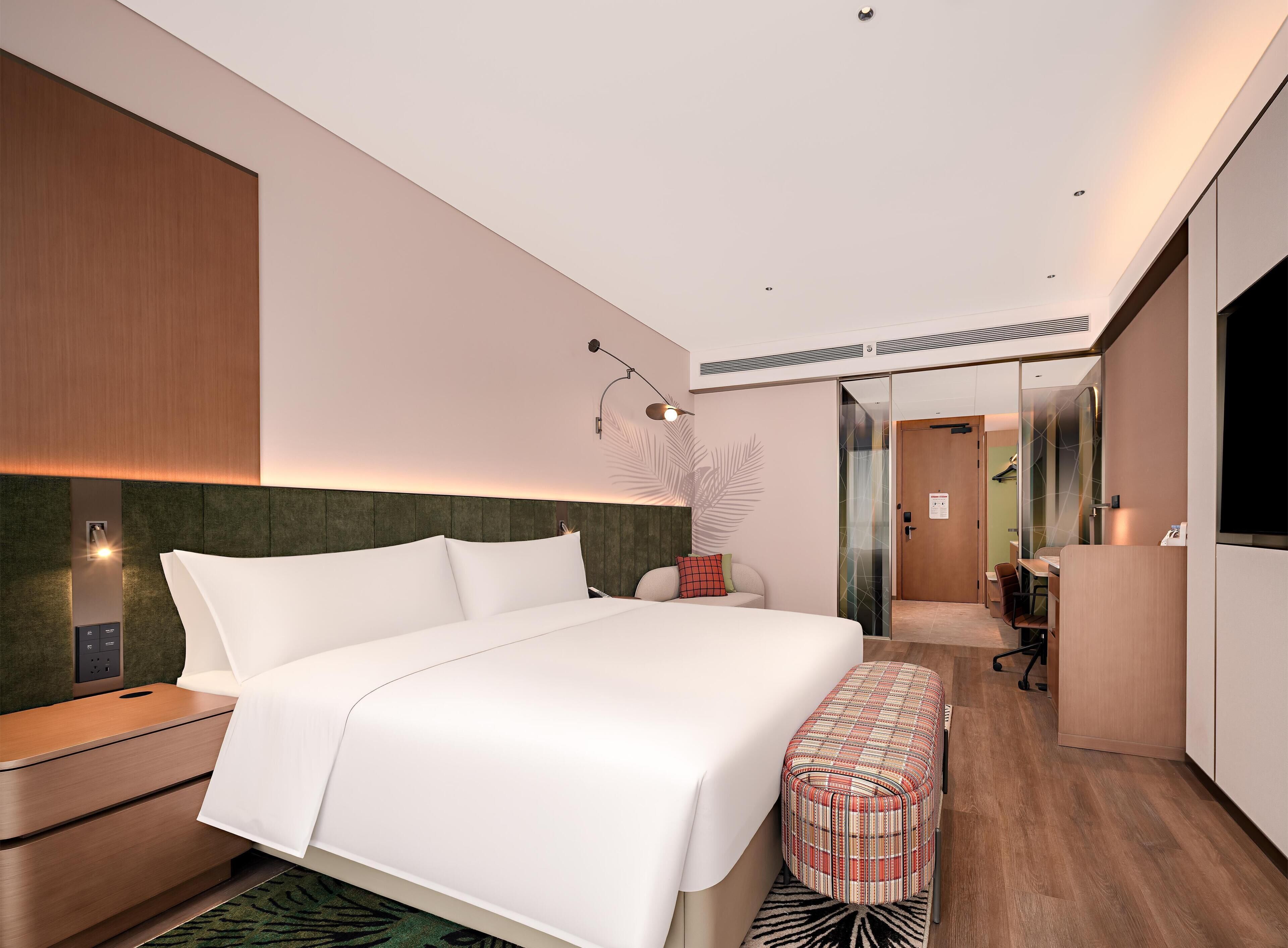 A modern hotel room with a large bed, a desk, a mirror, and a wardrobe.