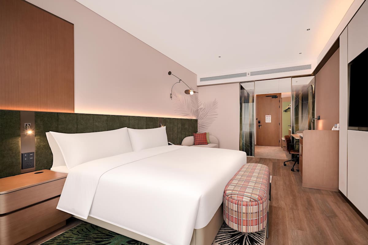A modern hotel room with a large bed, a desk, a mirror, and a wardrobe.