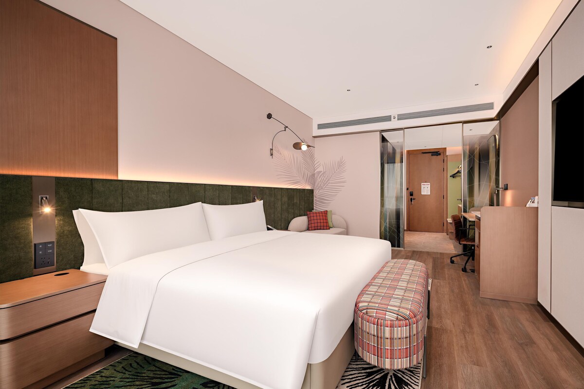 A modern hotel room with a large bed, a desk, a mirror, and a wardrobe.