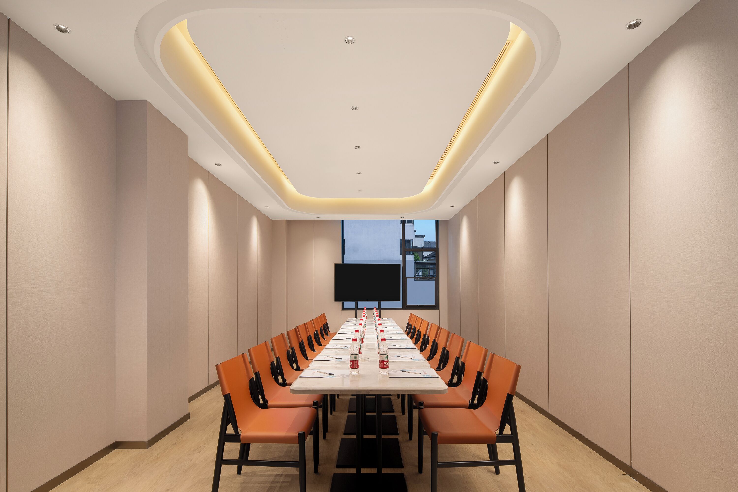 Ein Konferenzraum mit einem langen Tisch, orangefarbenen Stühlen und einer großen Leinwand im Vordergrund.