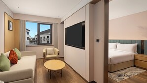 Una camera d'albergo moderna con divano, poltrona, tavolino rotondo e un letto con testiera.