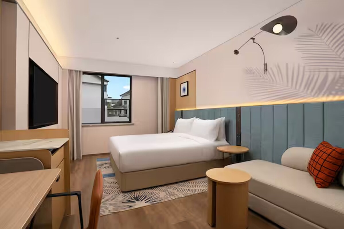 A modern hotel room with a bed, a desk, a sofa, and a small table.