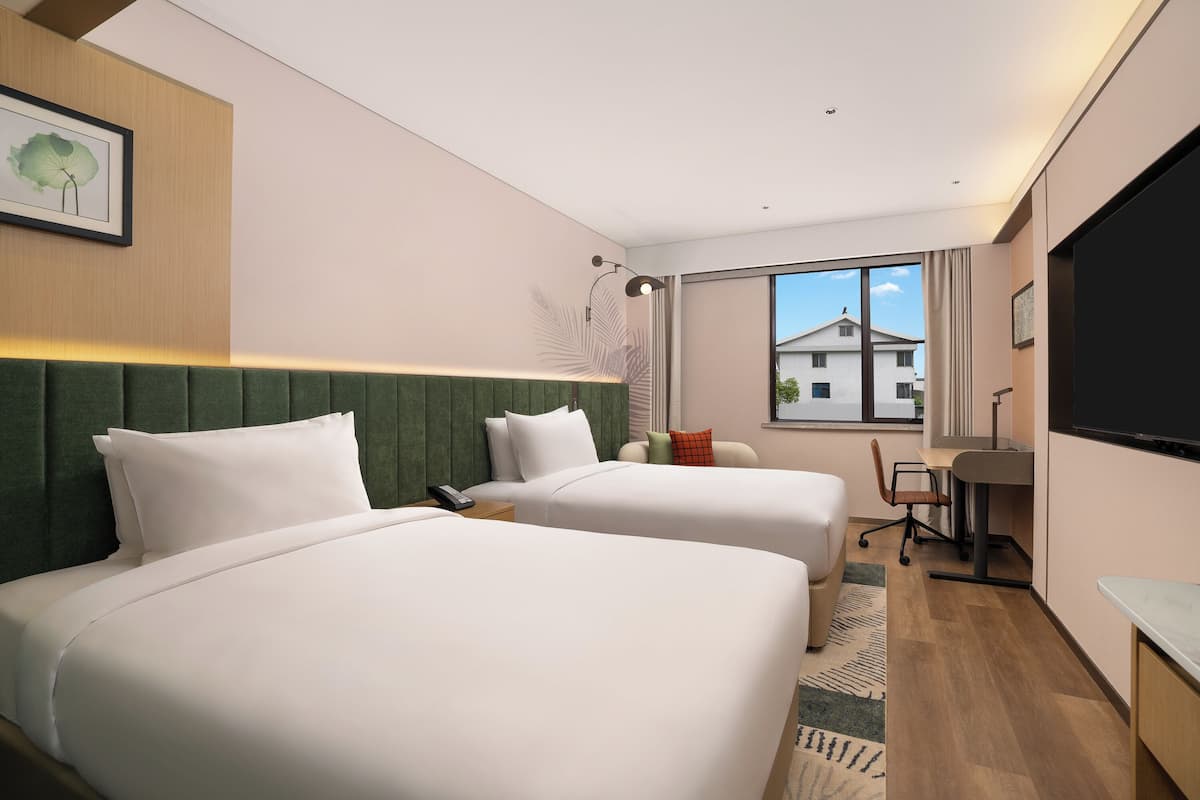 A hotel room with two beds, a desk, a chair, and a large window.