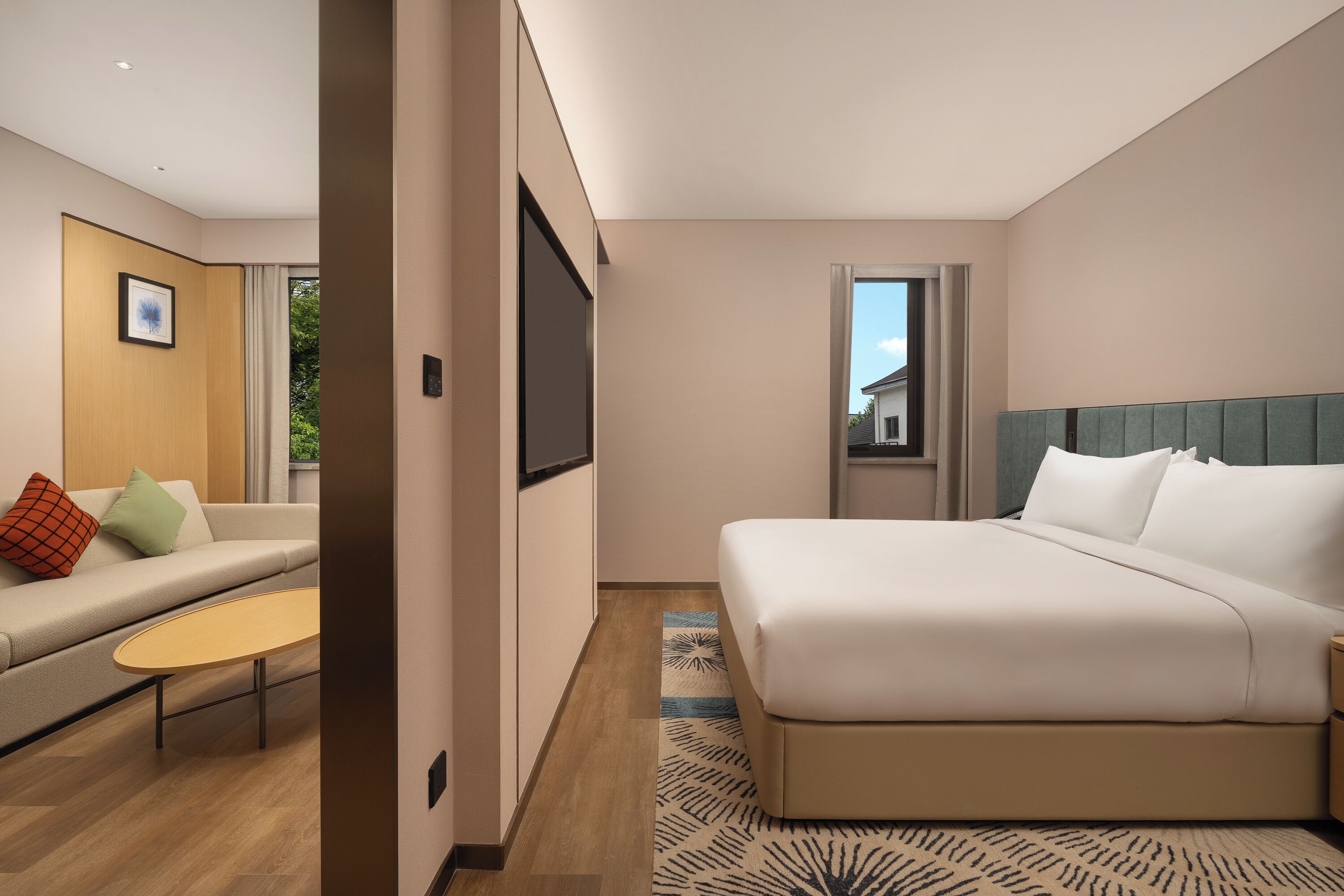 Una habitación de hotel moderna con una cama grande, un sofá, una mesita y un televisor.