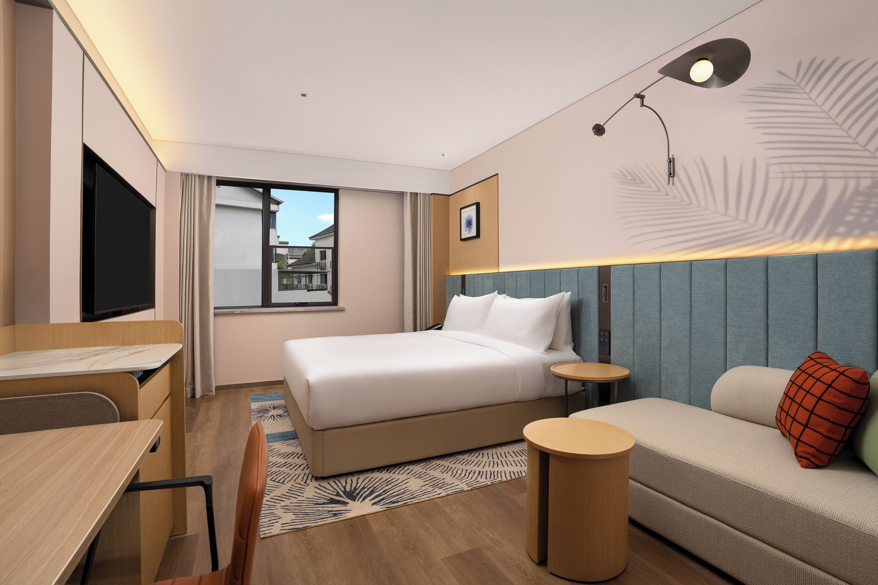 A hotel room with a bed, a desk, a sofa, a small table, and a TV.