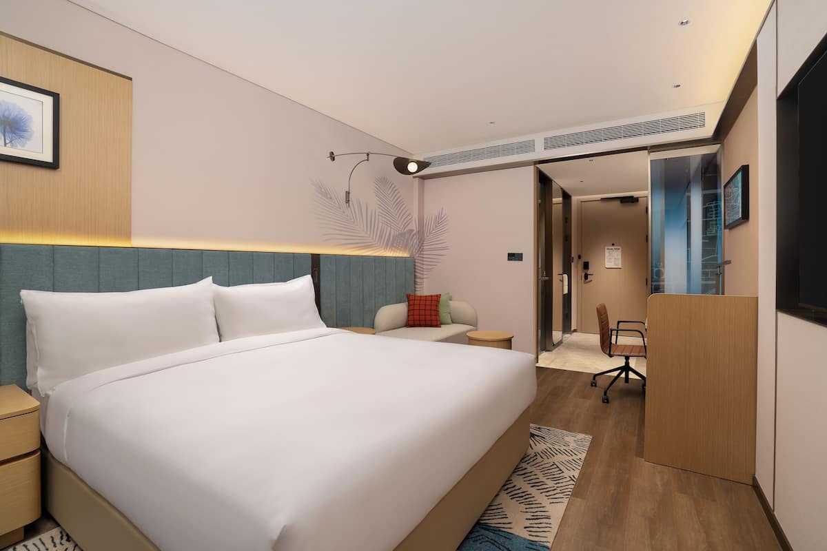 A modern hotel room with a large bed, bedside tables, a desk, and a chair.