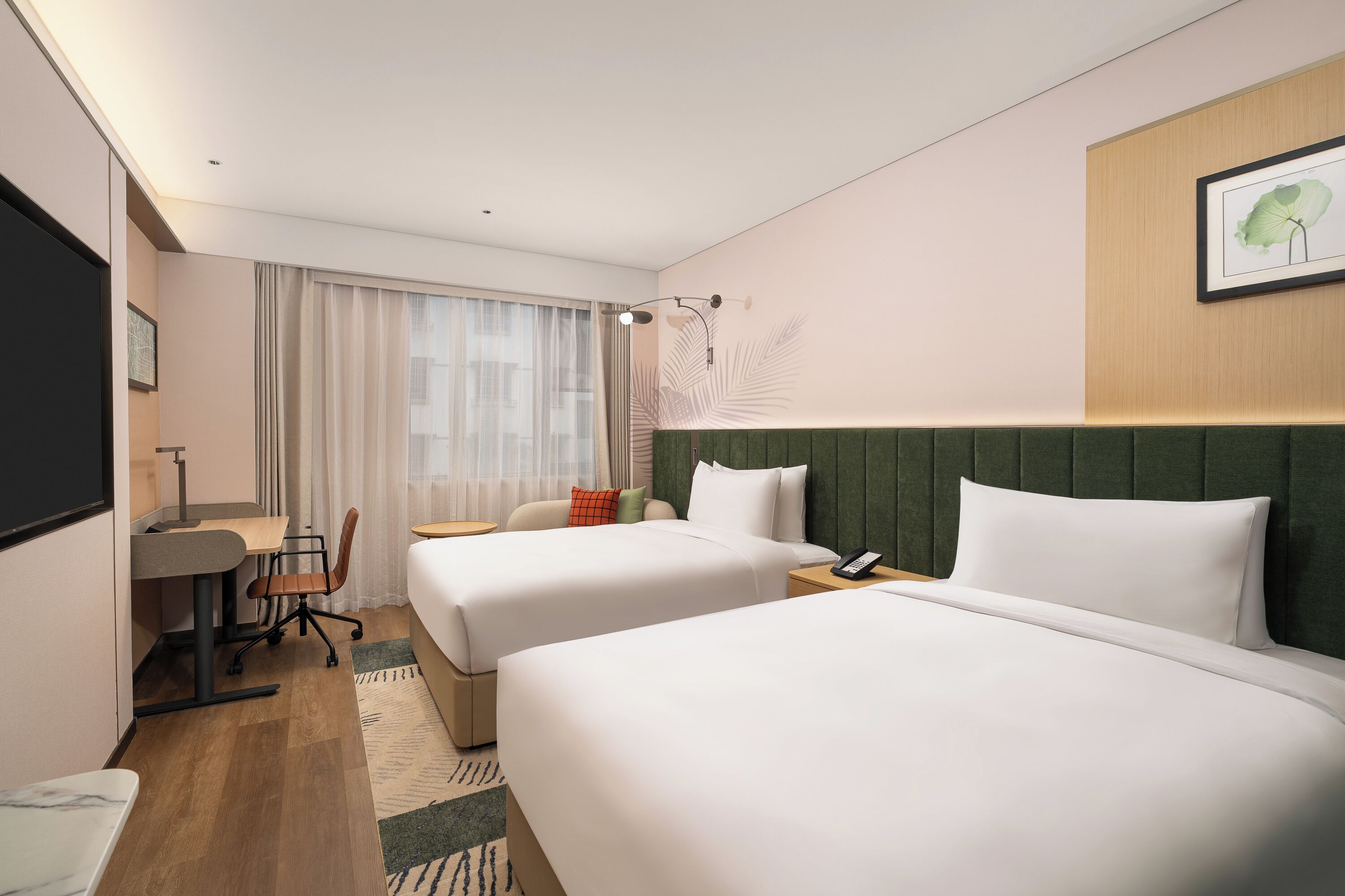 Habitación de hotel con dos camas, un escritorio con silla, una mesita pequeña y una mesita de noche con un teléfono.