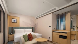 A modern hotel room with a bed, a sofa, a small round table, a vanity with a mirror, and a built-in wardrobe. - Hilton Garden Inn Shaoxing Lu Xun Native Place (Shaoxing)