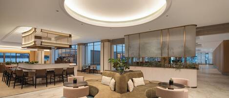 A modern lobby with a central seating area, a reception desk, and large windows offering views of the city.