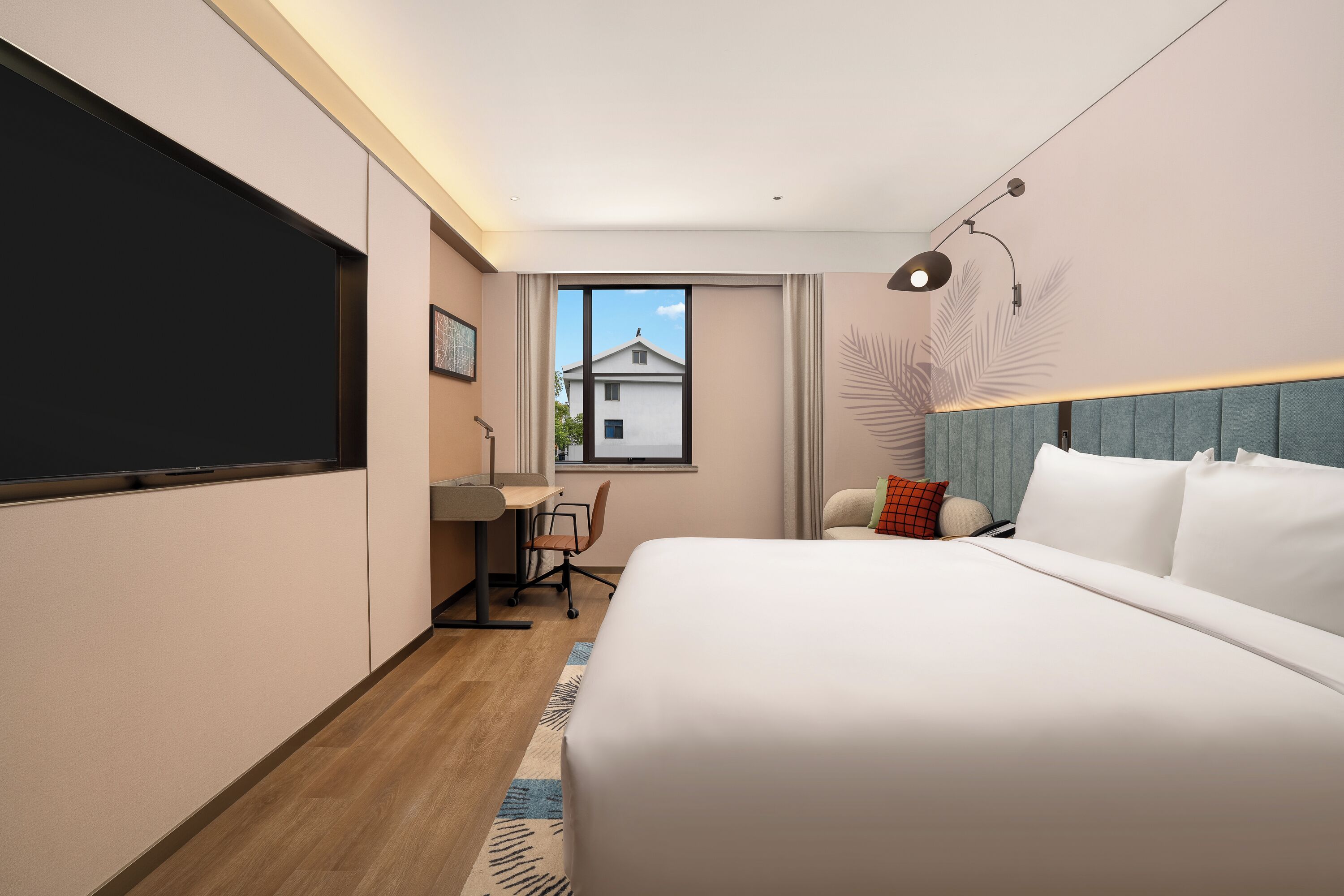 A modern hotel room with a large bed, a desk, and a window with a view of a building.