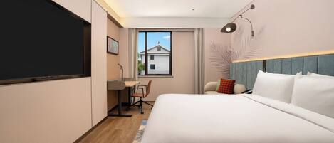 A modern hotel room with a large bed, a desk, and a window with a view of a building.