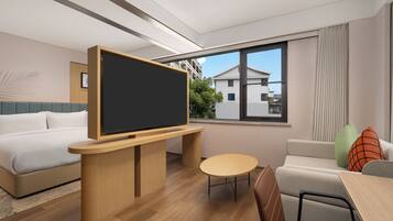 A modern hotel room with a bed, a desk with a flat-screen TV, a small round table, and a sofa.